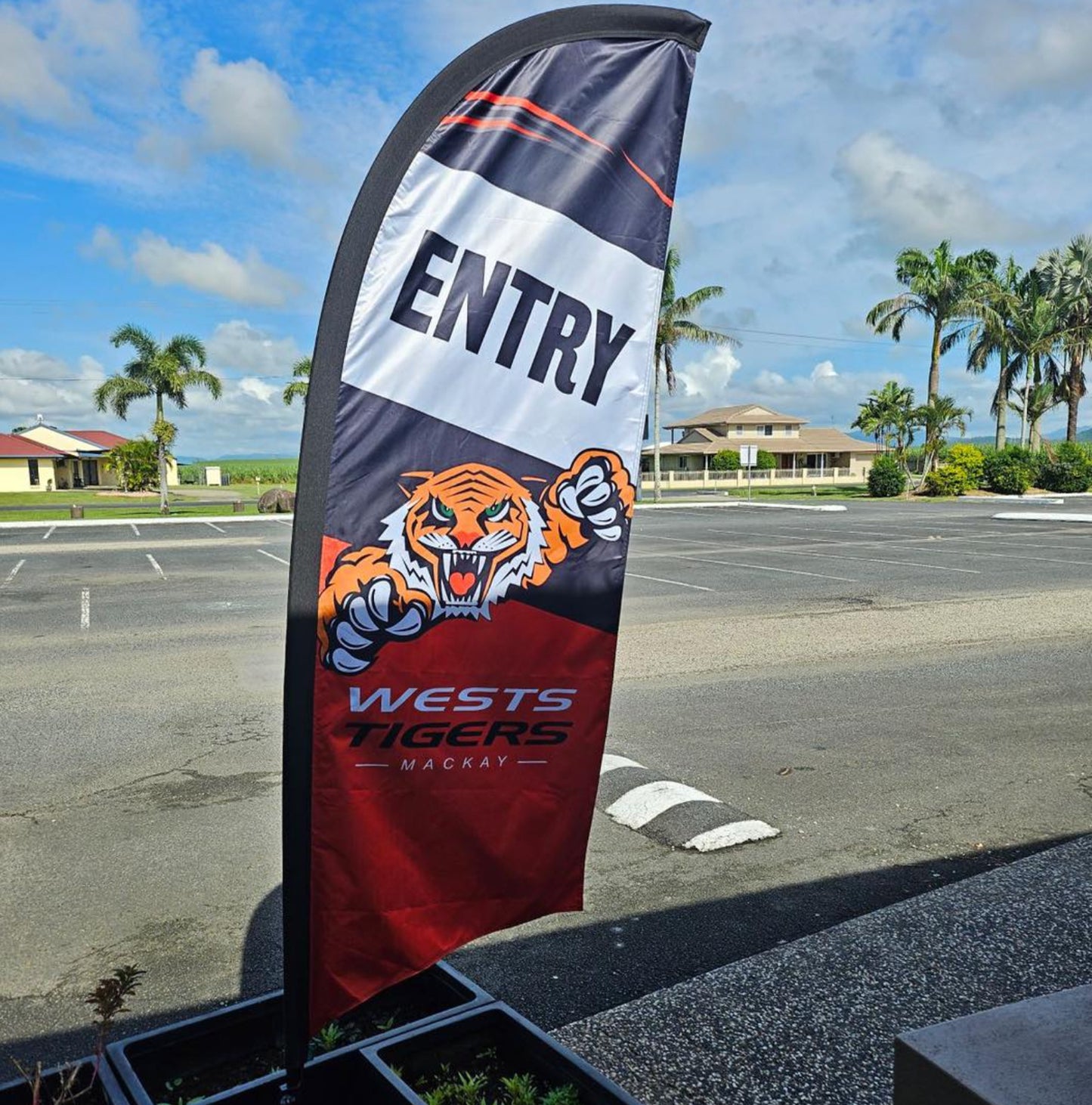 Teardrop flag with 'Entry' and Wests Tigers logo in a parking lot.